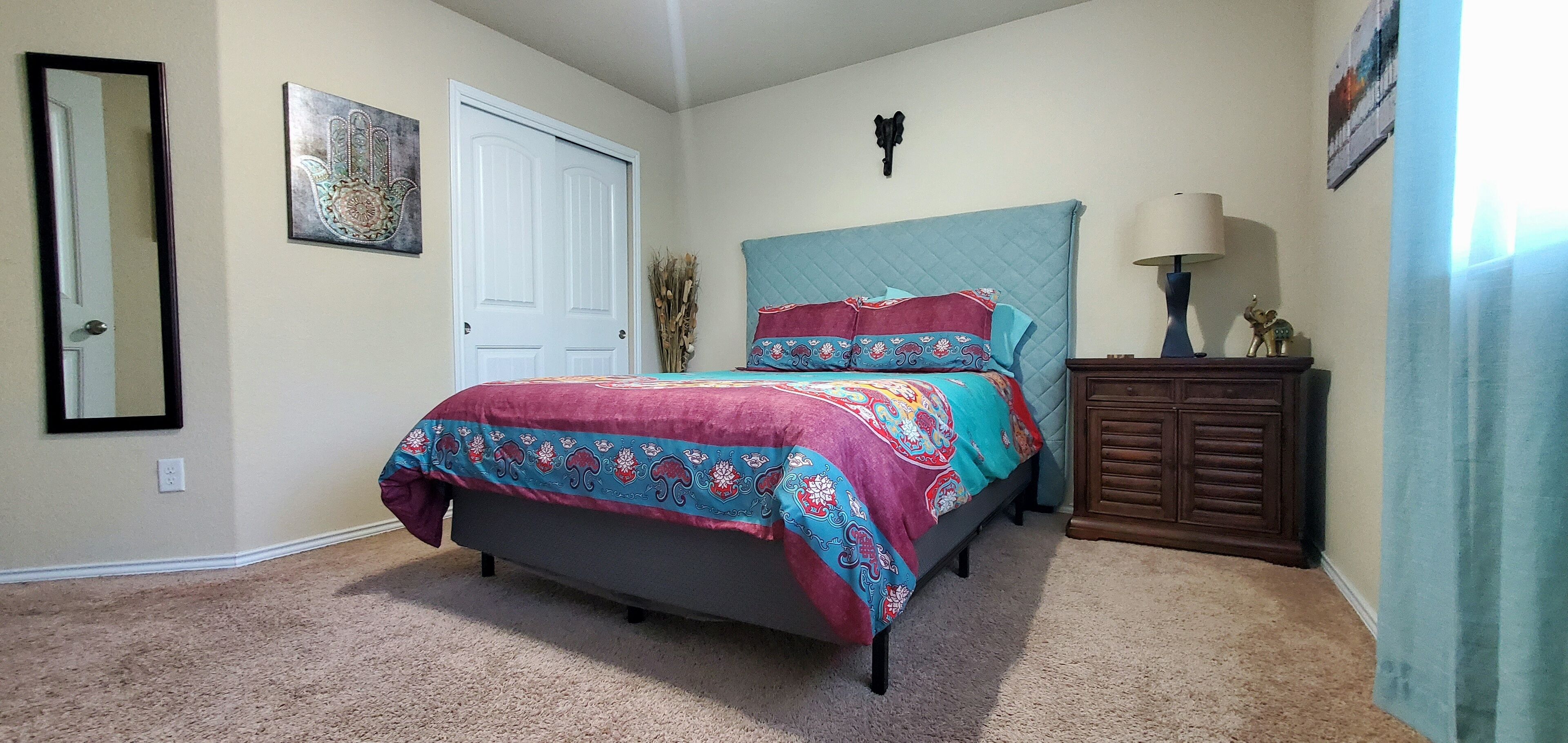 Une chambre à coucher avec un lit, une commode, un miroir et une porte.