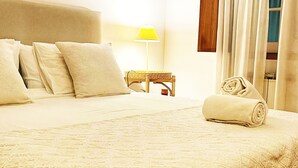 A neatly made bed with a rolled towel, a bedside lamp, and a small wooden table with a lamp.