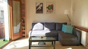 Uma sala de estar com um sofá, uma mesa de centro de vidro e dois quadros na parede.