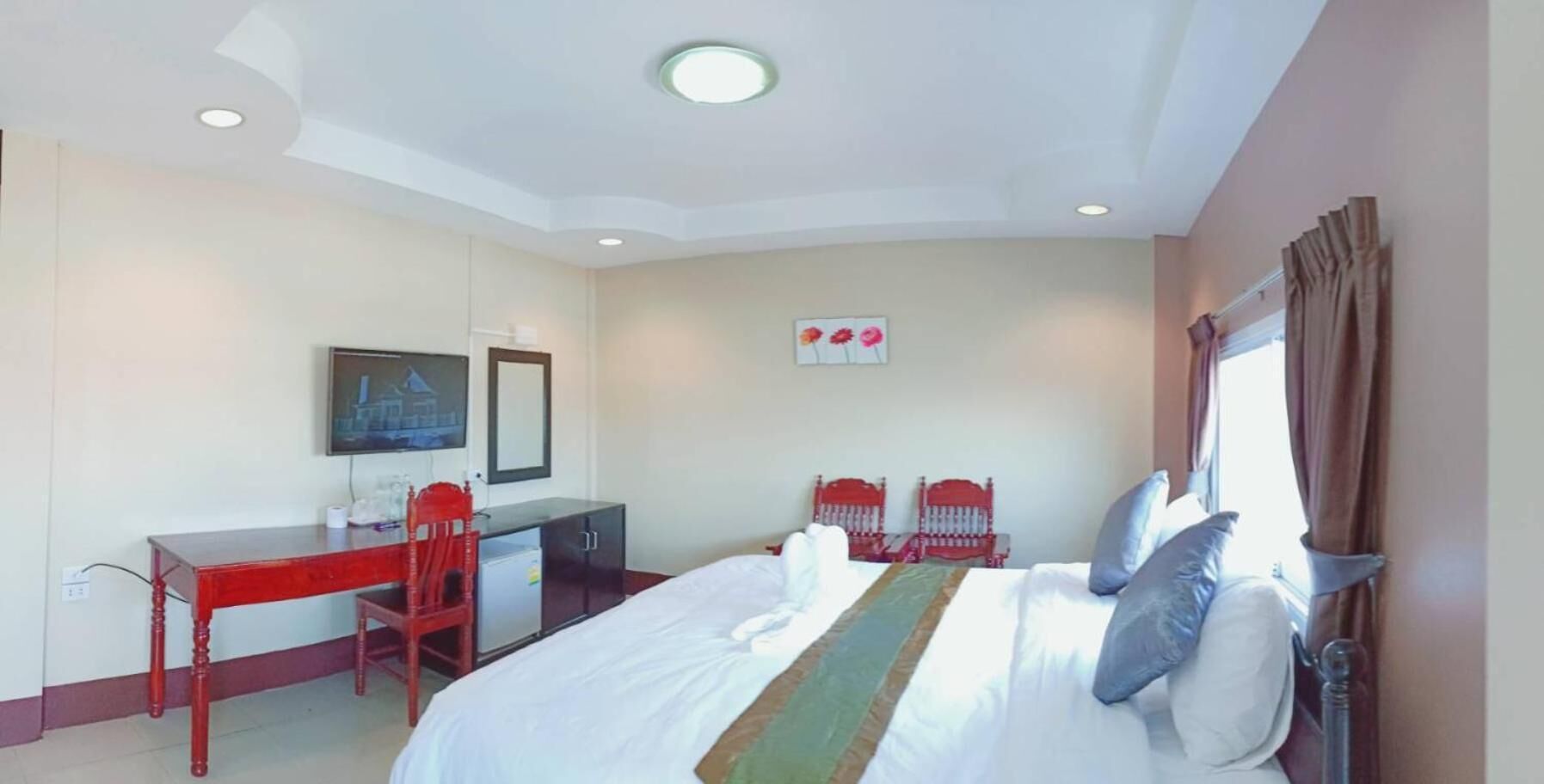 A hotel room with a large bed, a desk, two chairs, a television, and a window with curtains.