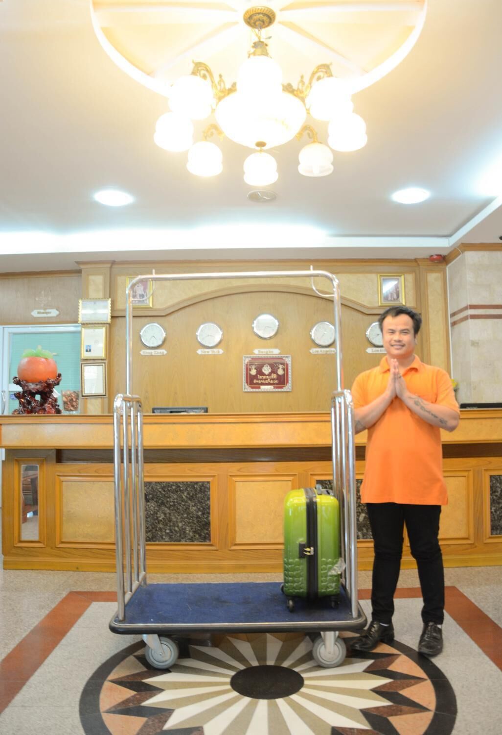 A hotel reception area with a wooden counter, a chandelier, clocks, and a luggage cart.