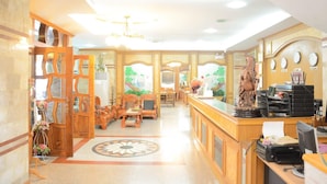 A hotel lobby with a reception desk, wooden furniture, a decorative horse statue, and a large window with a view of greenery. - Submukdaphoomplace Hotel (Mukdahan)