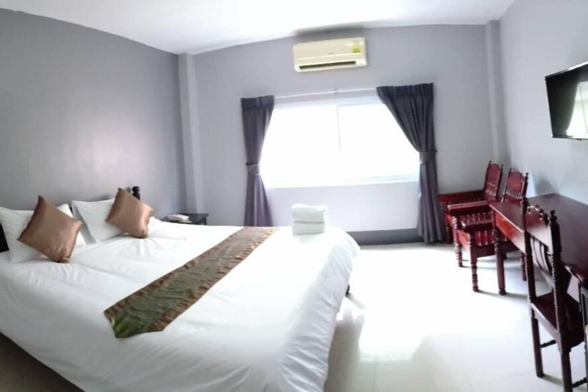 A hotel room with a large bed, a desk, a chair, a TV, and a window with curtains.