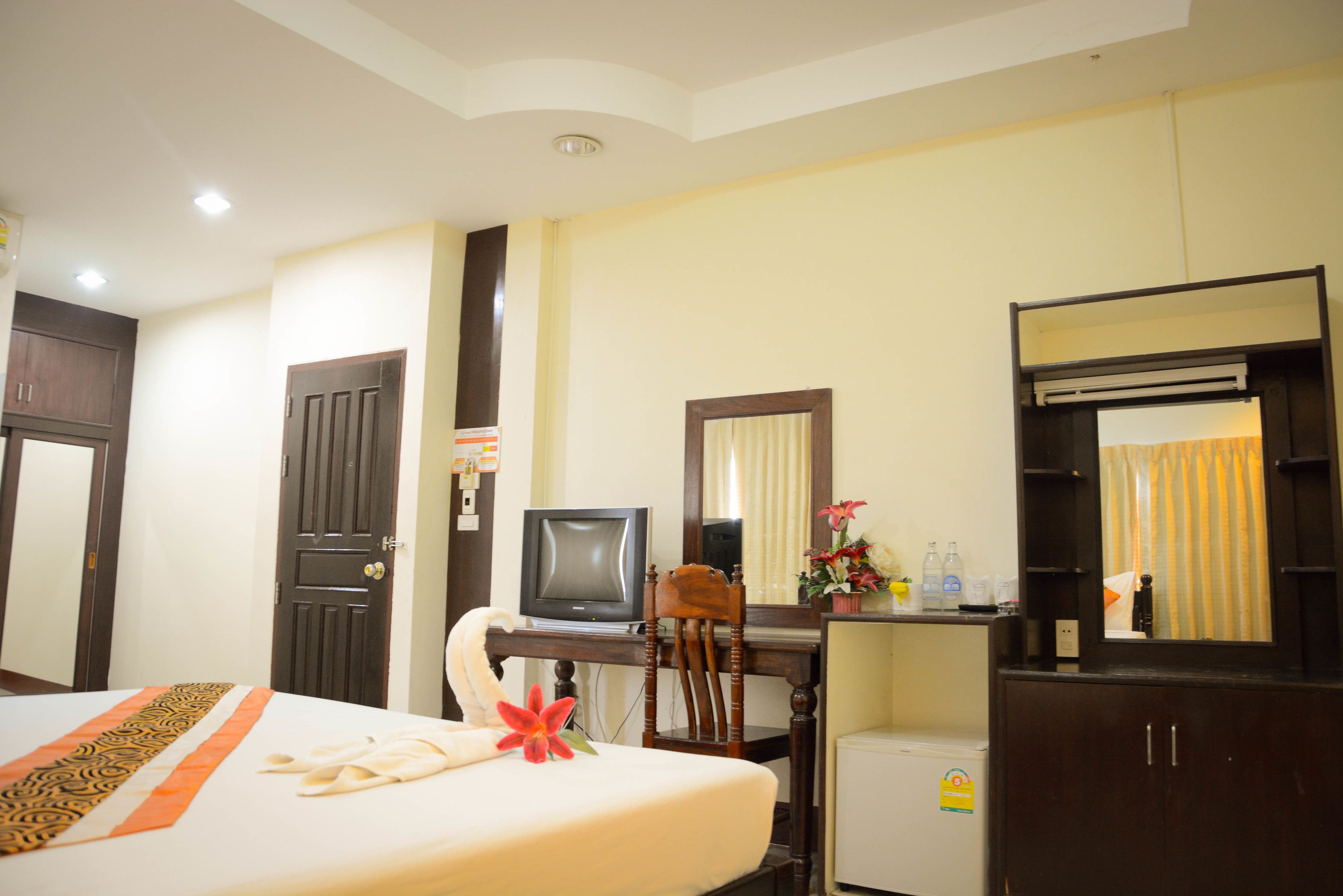 A hotel room with a bed, a desk with a television, a small refrigerator, and a mirror.
