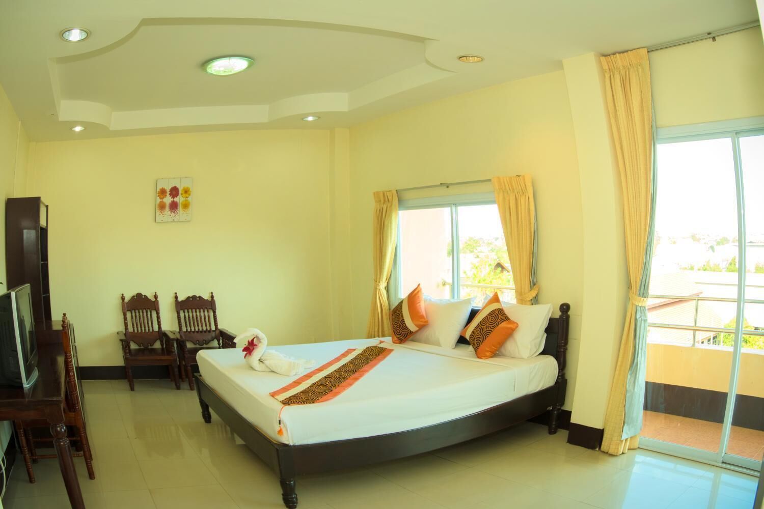 A hotel room with a large bed, two wooden chairs, a television, and a window with curtains.