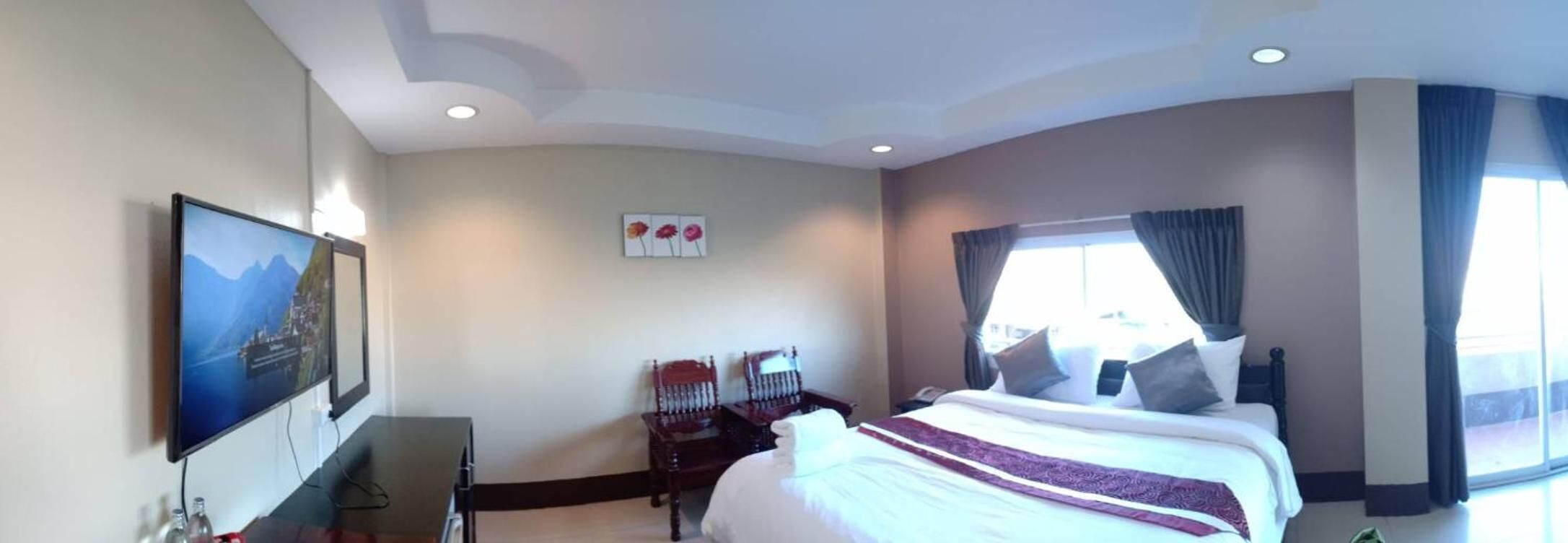 A hotel room with a large bed, a desk, a chair, and a window with curtains.