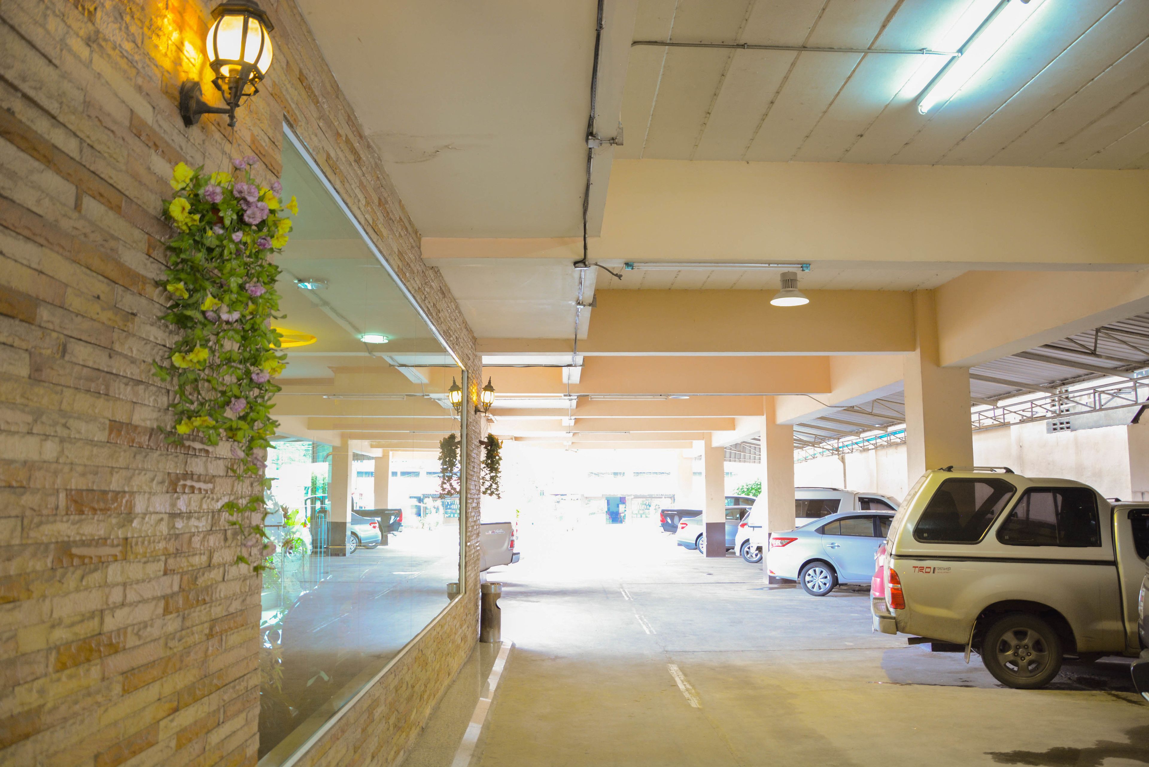 A parking garage with brick walls, hanging floral decorations, and multiple parked vehicles.
