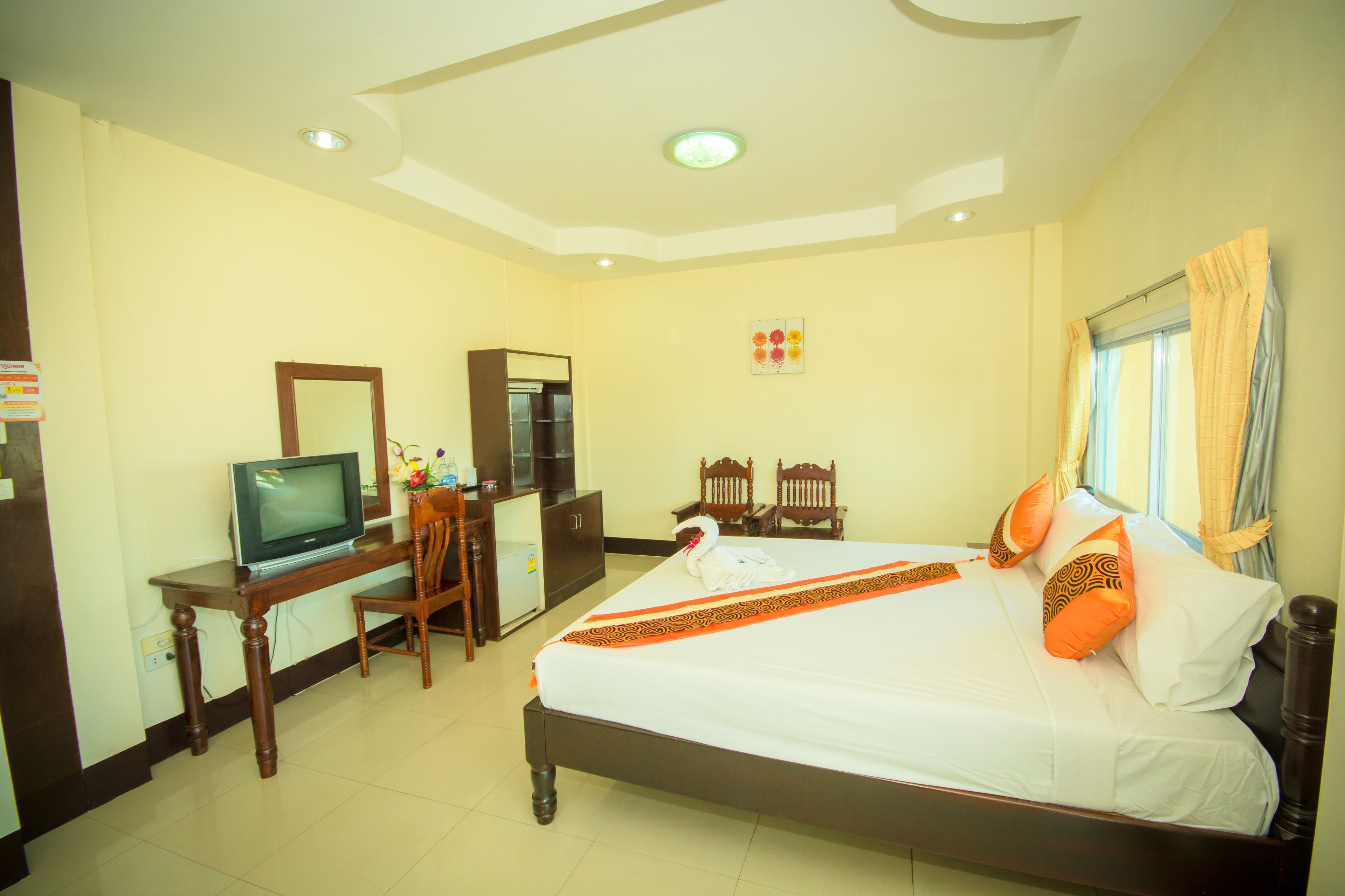 A hotel room with a bed, a desk with a television, a small refrigerator, and a window with curtains.