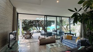 A spacious living area with a high ceiling, large windows, and a view of the outdoors.