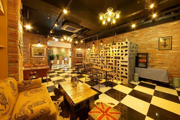 Un café chaleureux avec un sol à carreaux, des murs en briques et différents types de sièges, notamment des tables et des chaises.