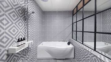 A modern bathroom with a geometric patterned wall, a large bathtub, and a mirror with a black frame.