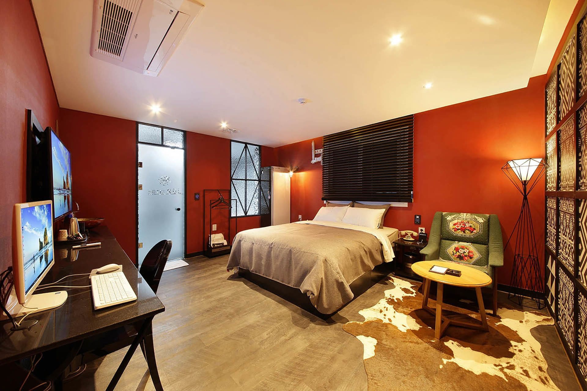 A modern bedroom with a bed, a desk with a computer, a chair, and a decorative rug.