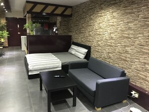A modern room with a sofa bed, a small table, and a stone wall. - Halz city estates (London)