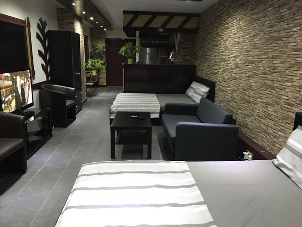 A modern living room with a sofa, a bed, and a television. There are plants and a kitchen in the background. - Halz city estates (London)