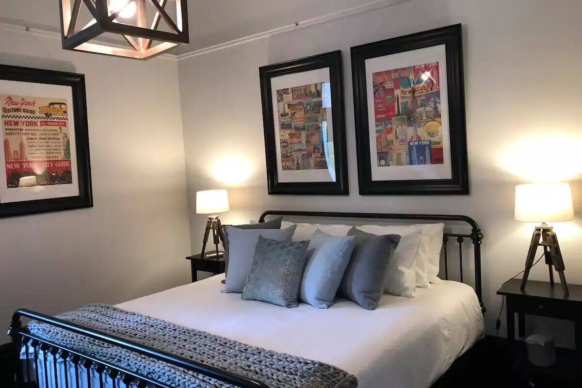 Quarto de hotel bem arrumado, com uma cama grande, dois cartazes emoldurados na parede e abajures nas mesas de cabeceira.