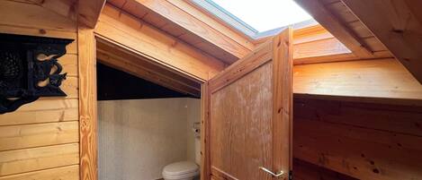 Une petite chambre mansardée en bois, avec un puits de lumière, des toilettes et une armoire en bois.