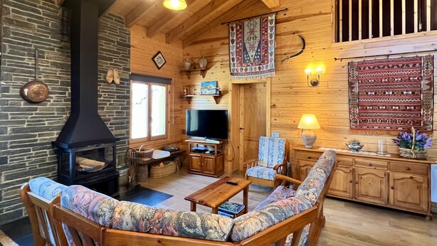 Ein gemütliches Blockhäuschen mit Kamin aus Stein, Holzmöbeln und einem Fernseher.
