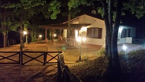 Ein Nachtbild von einem Haus mit überdachter Terrasse, einem kleinen Pool und einem umzäunten Eingang.
