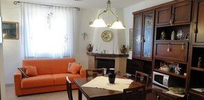 A living room with a sofa, a dining table, and a fireplace. There are cabinets with various items and a television.
