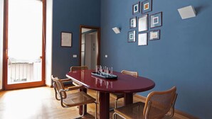 Zona pranzo con un tavolo ovale rosso, quattro sedie in vimini e quadri appesi alle pareti.