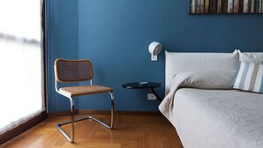 Una camera da letto con un letto, una sedia, un tavolino e una lampada a parete.