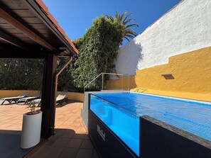 Una piscina con superficie de agua cristalina azul, rodeada de una zona de solárium con baldosas.