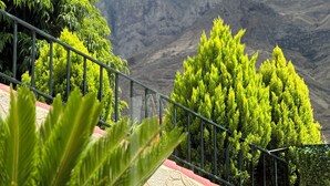 Una escalera con barandillas de metal que asciende por un sendero de montaña, rodeada de árboles verdes y con montañas rocosas al fondo.