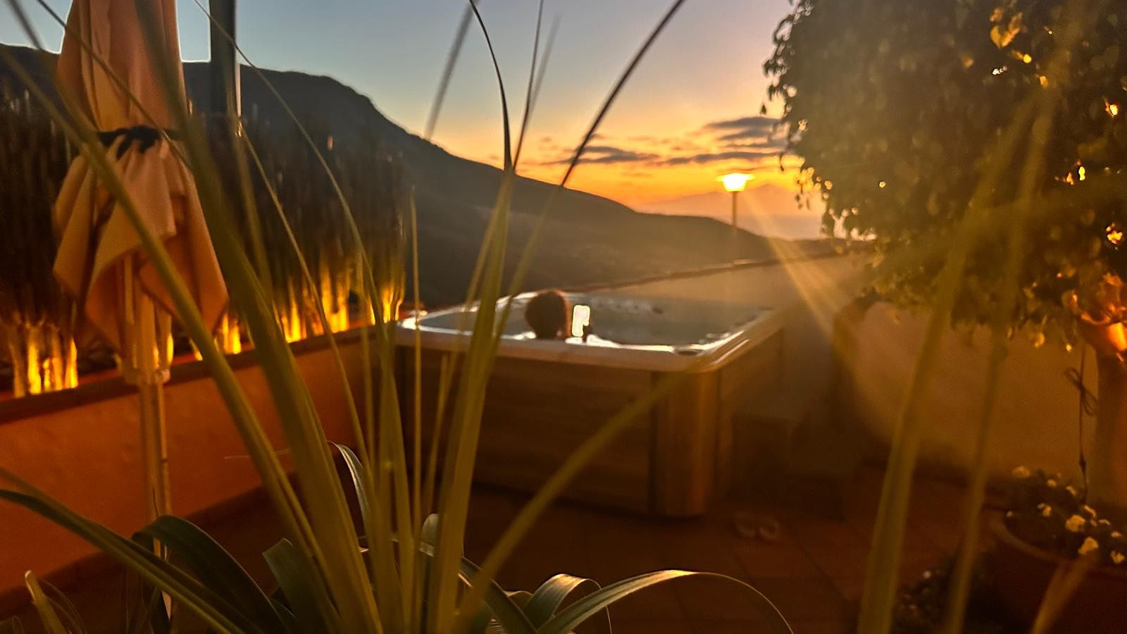 A hot tub with a view of the sunset and mountains in the background.