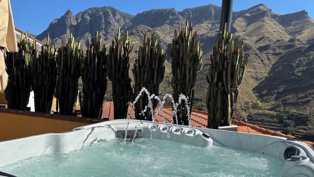 Un jacuzzi con chorros de agua, rodeado de cactus y montañas al fondo.