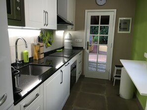 Cocina compacta con lavabo, estufa y armarios. Una puerta da a un espacio exterior con vistas a zonas verdes.