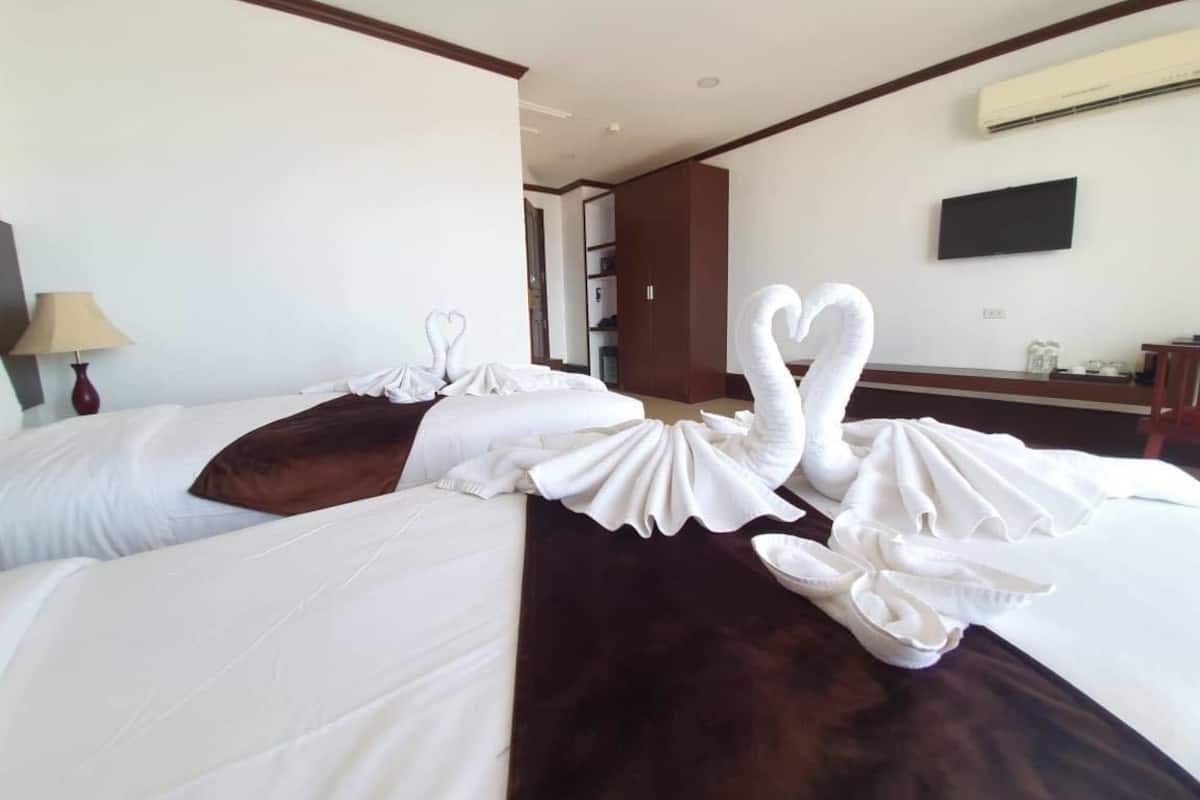 Habitación de hotel con dos camas, cada una decorada con almohadas en forma de cisne blanco y una manta marrón.
