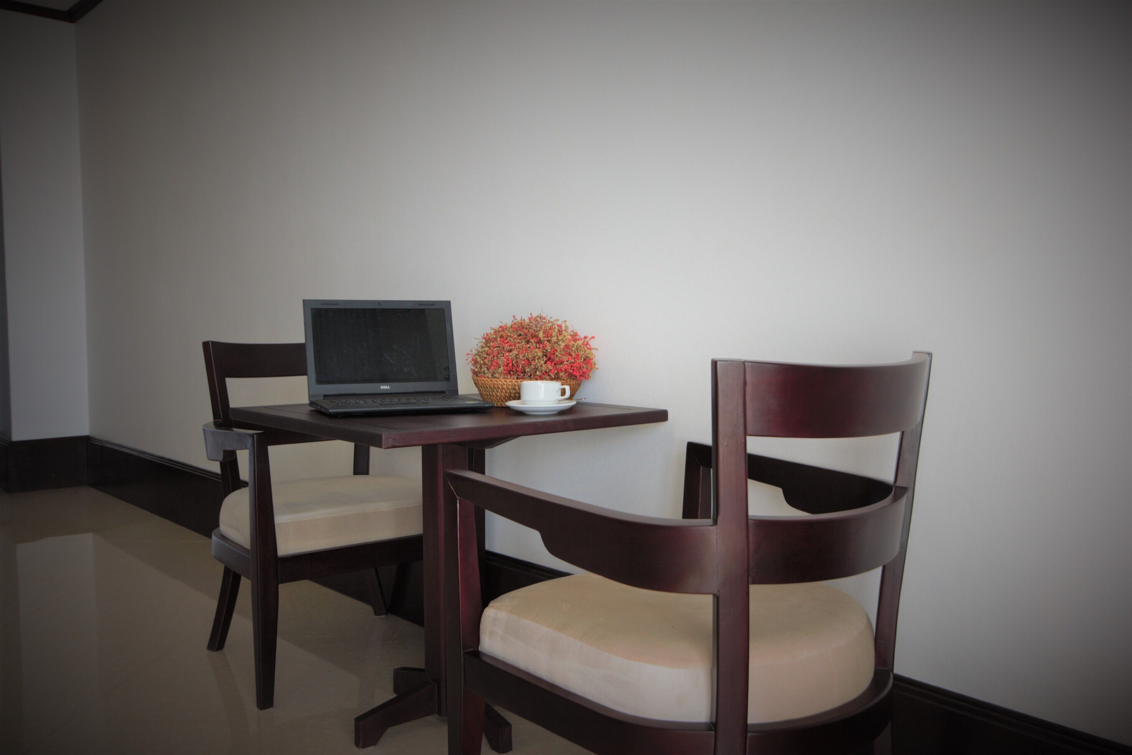 A room with a desk, laptop, and two chairs.