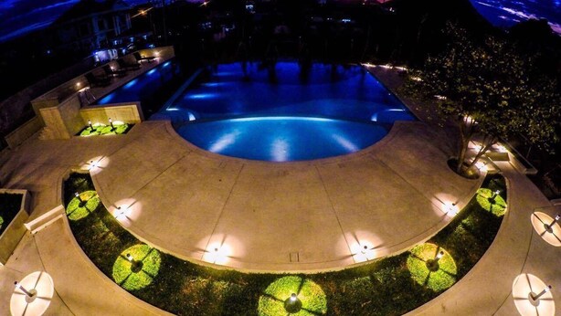 Zona de piscina circular al aire libre con una fuente central, rodeada por un muro bajo con luces uniformemente distribuidas.