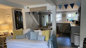 A cozy living room with a white sofa, a dining table, and a kitchen area with a refrigerator and sink. - Beautiful Holiday Cottage next to beach in Cawsand, SE Cornwall - dog friendly! (Cawsand)