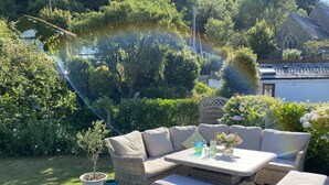 A covered outdoor seating area with a wicker sofa, a table, and a small potted plant. - Beautiful Holiday Cottage next to beach in Cawsand, SE Cornwall - dog friendly! (Cawsand)