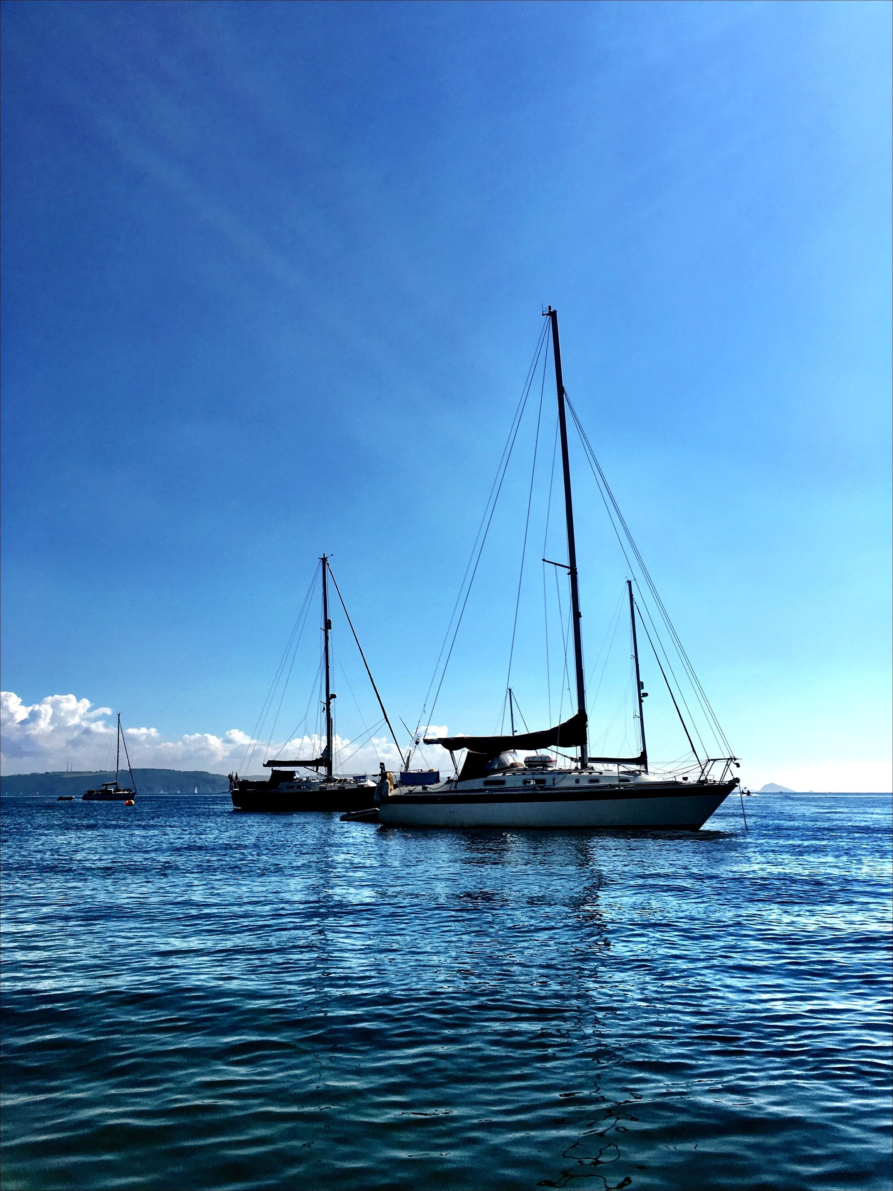 Un voilier est amarré dans une marina, sur des eaux calmes, sous un ciel dégagé.
