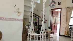Um quarto espaçoso com uma cadeira de macramê suspensa, um tapete redondo tecido e uma escada que leva a um andar superior.