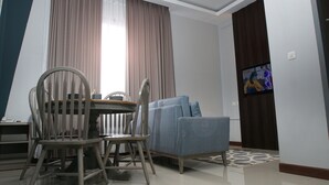 Una sala de estar con una mesa de comedor, sillas, un sofá y un televisor montado en la pared.