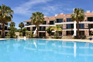 A swimming pool surrounded by multi-story buildings with balconies and palm trees.
