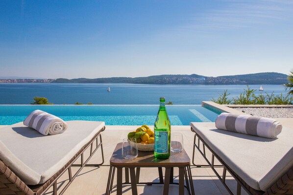 Une vue sur la piscine avec deux chaises longues, une table sur laquelle se trouvent une bouteille d’eau, un bol de citrons et des verres.