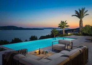 Un espace aménagé au bord de la piscine, avec vue sur la mer, comprenant un canapé et une table avec des boissons.