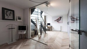 Een modern interieur met een visgraat parketvloer, een flatscreen televisie, ingelijste kunstwerken en een trap die naar een hoger niveau leidt.