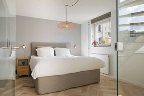 A modern bedroom with a bed, bedside lamps, a window, and a view of the outside.