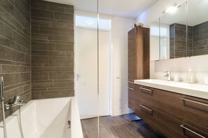 A modern bathroom with a bathtub, a wooden vanity, and a large mirror.