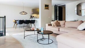 Een moderne woonkamer met een beige bank, twee ronde salontafels en een eethoek met een tafel en stoelen.