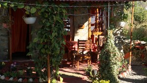 A rustic outdoor seating area with a wooden table and chairs, surrounded by potted plants and a stone wall. - The Mapple Cottage (Nainital)