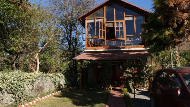 A two-story wooden house with a balcony, surrounded by trees and a garden. - The Mapple Cottage (Nainital)
