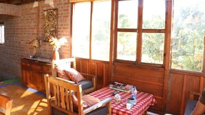 A rustic wooden cabin with a dining area, a sofa, and a table set with books and a teapot. - The Mapple Cottage (Nainital)