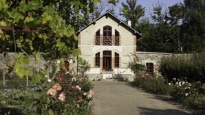 A two-story stone building with a central entrance, surrounded by a garden with various plants and flowers. - In Anjou in the castle vegetable garden, Peace, flower and vegetable (Marans)