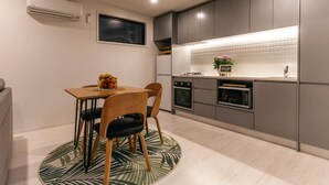 A modern kitchen with grey cabinets, a built-in oven, and a microwave. There is a dining table with chairs and a fruit bowl. - Guest House on Queens (Waiheke Island)
